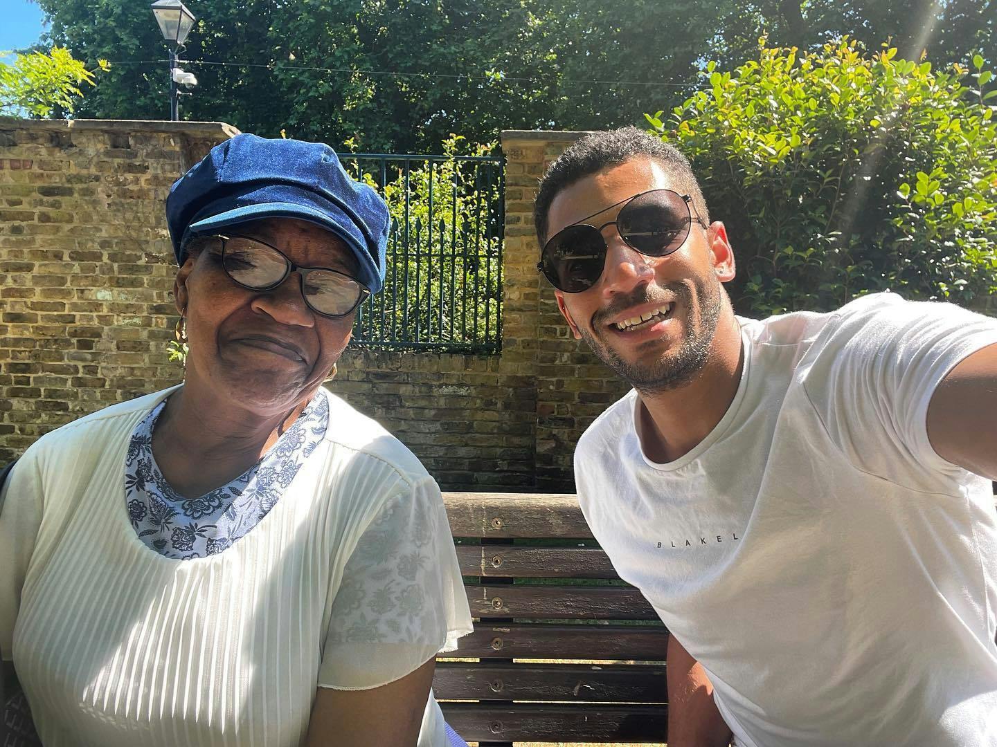 A younger and an older neighbour taking a selfie of themselves while sitting on a bench outside