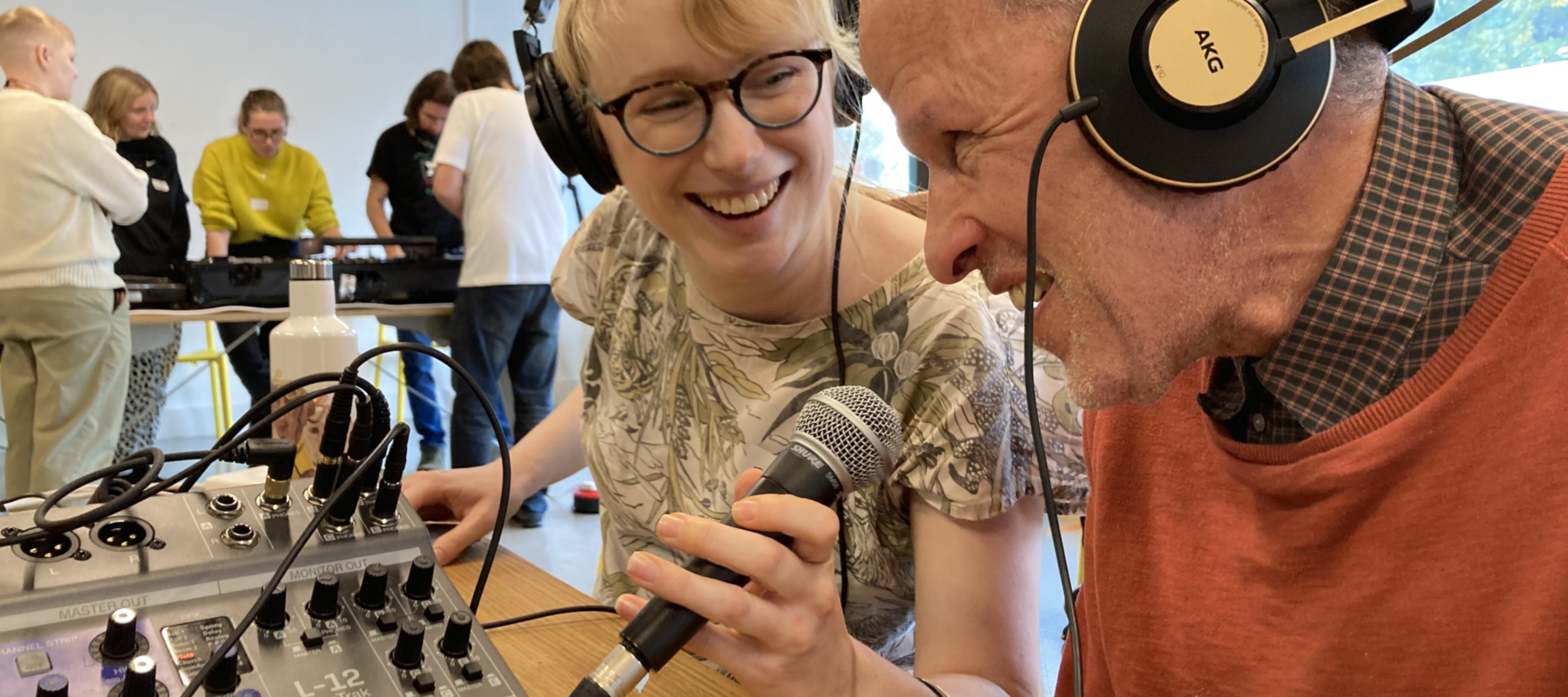 A younger and an older neighbour using recording equipment and laughing